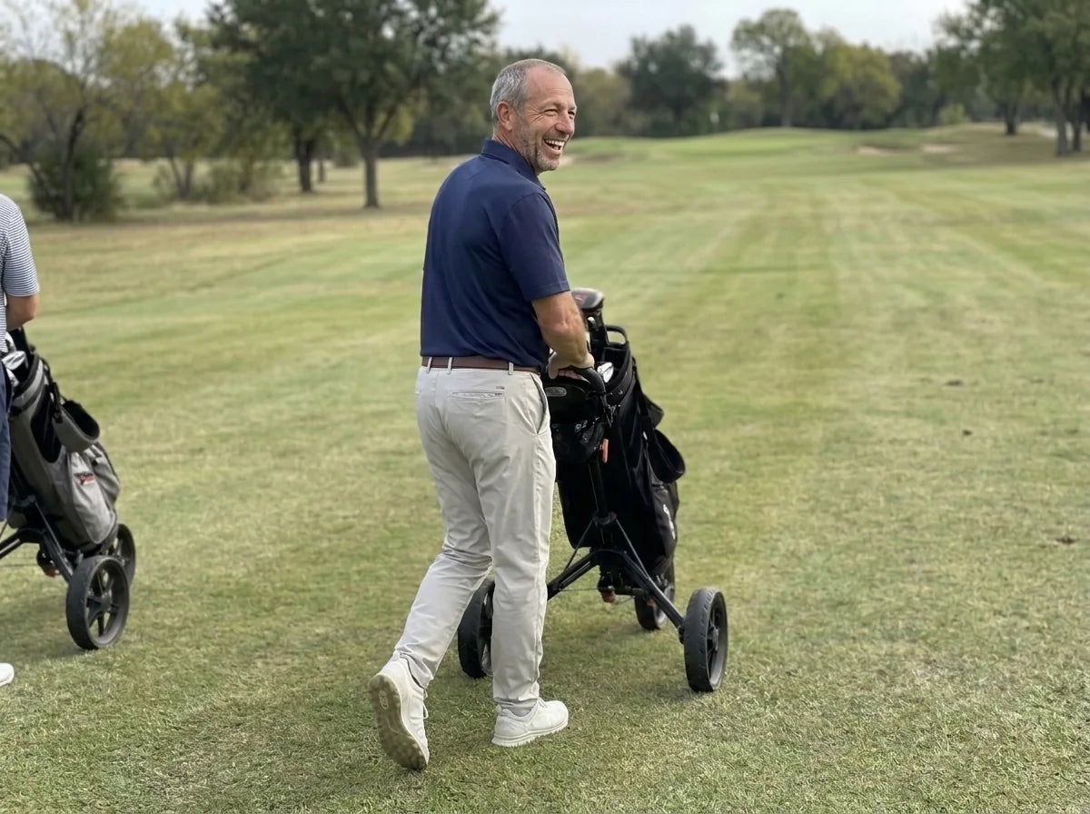 Greg laughing with his buddies as he walks the fairway with his push cart